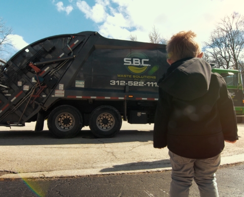 A little boy watch an SBC Waste Solutions truck in front of his house