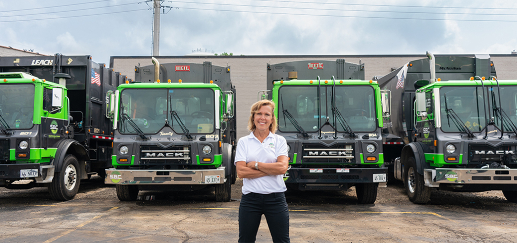 Karen, owner of S.B.C. Waste Solutions, standing in front of her waste trucks that provide waste management solutions