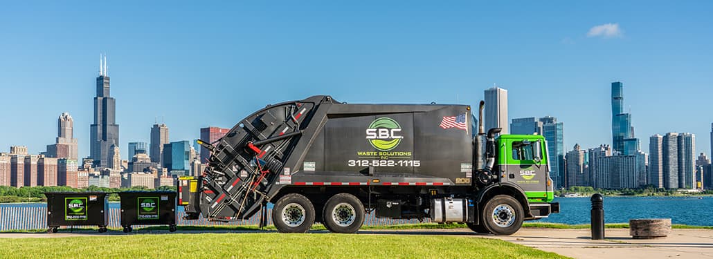 A large waste truck with a rear load dumpster positioned in front of the iconic Chicago skyline.